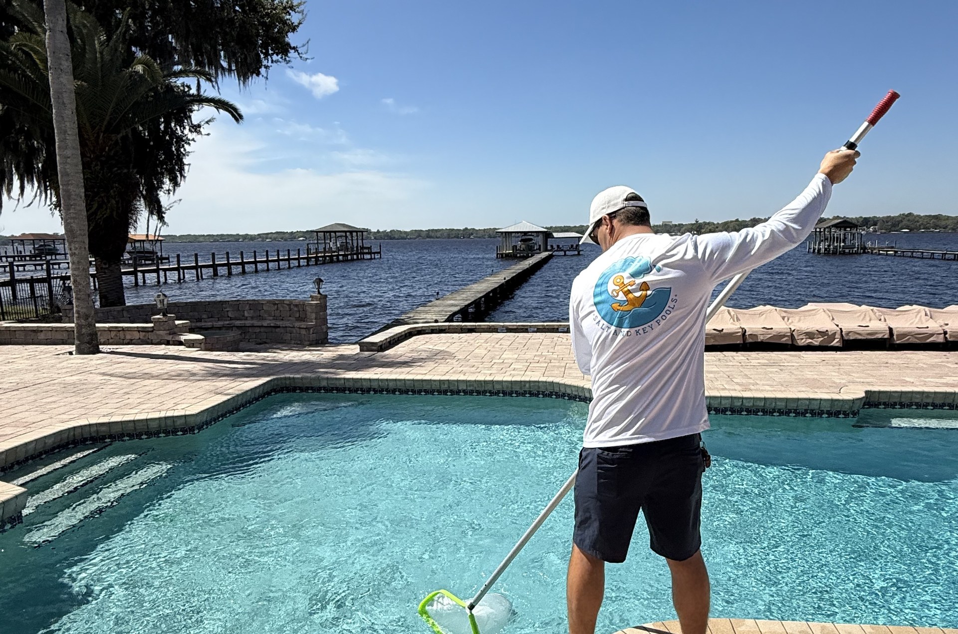 Salt and Key Pools technician skimming a waterfront backyard pool on the St. Johns River in Jacksonville, Florida